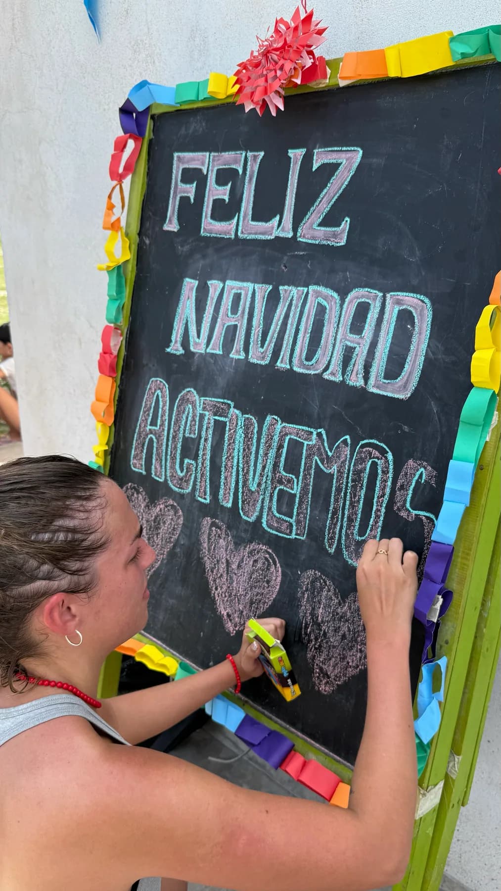 Una persona escribe un saludo de Navidad de ACTIVEMOS en una pizarra con marco de colores.